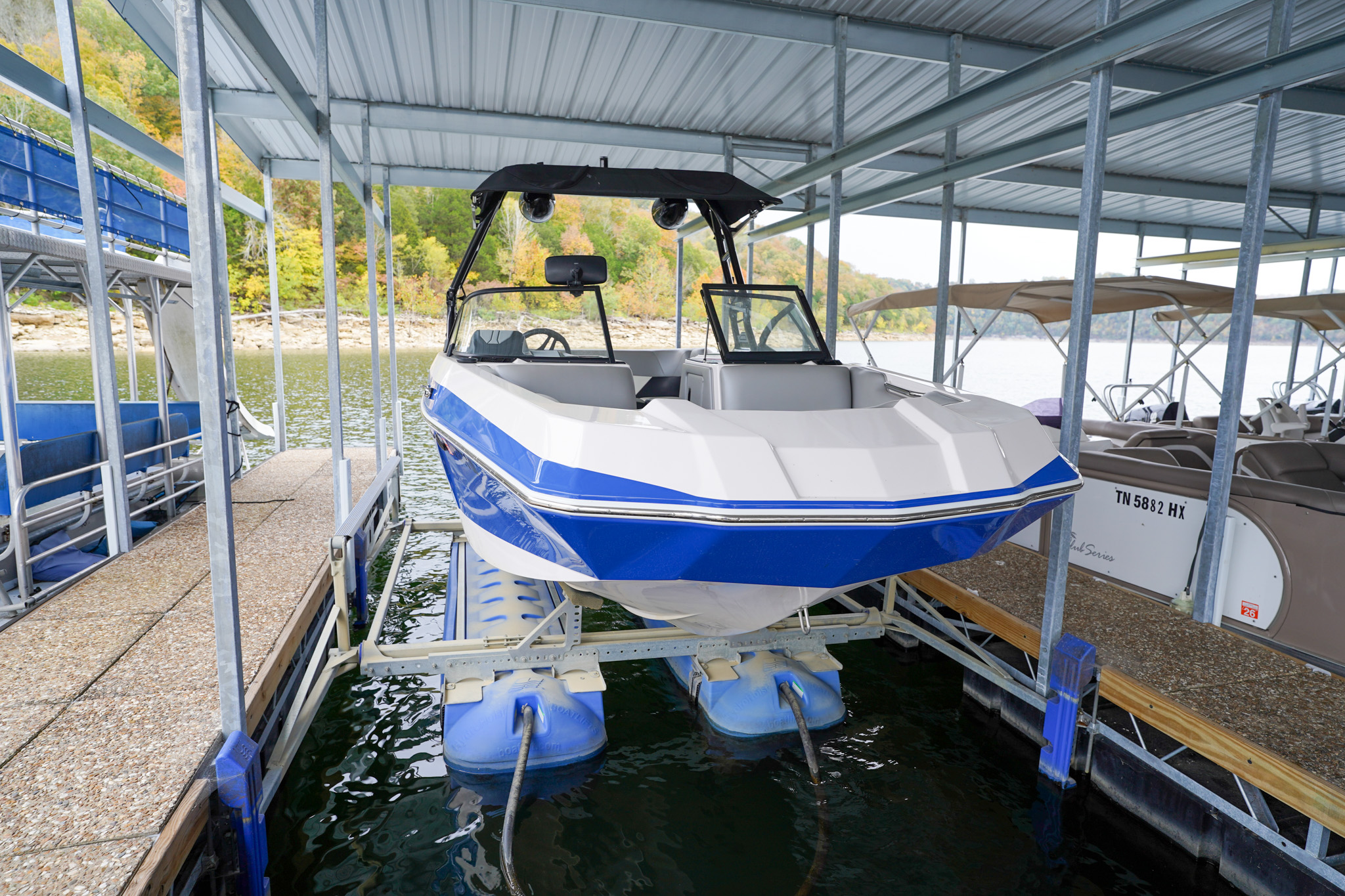 A blue and white speedboat resting on a floating boat lift under a covered marina.