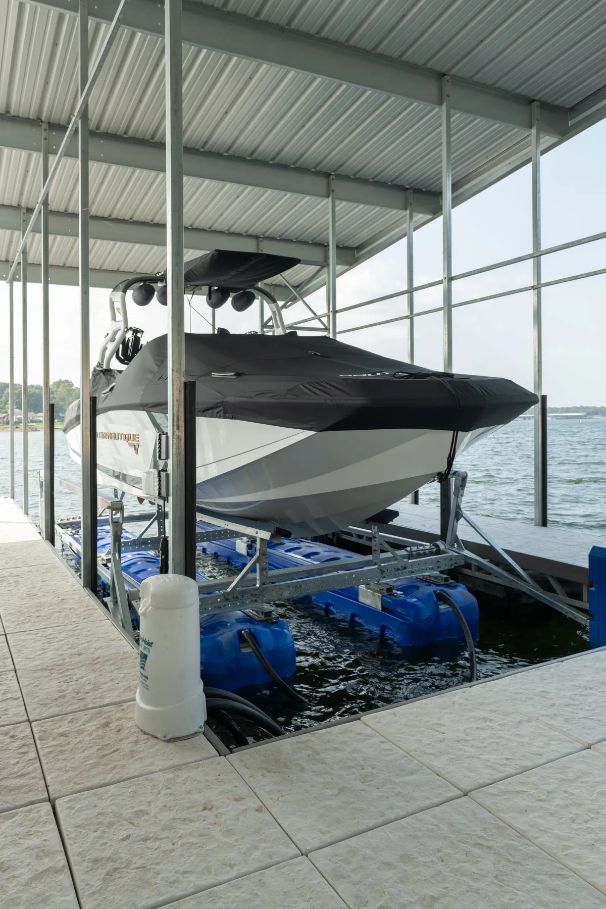 Covered Nautique boat lifted above the water on a floating dock lift at a lakeside marina