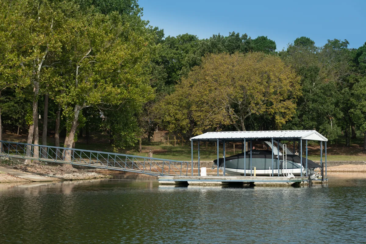 Covered boat dock with a boat lift and walkway on a tree-lined lake.
