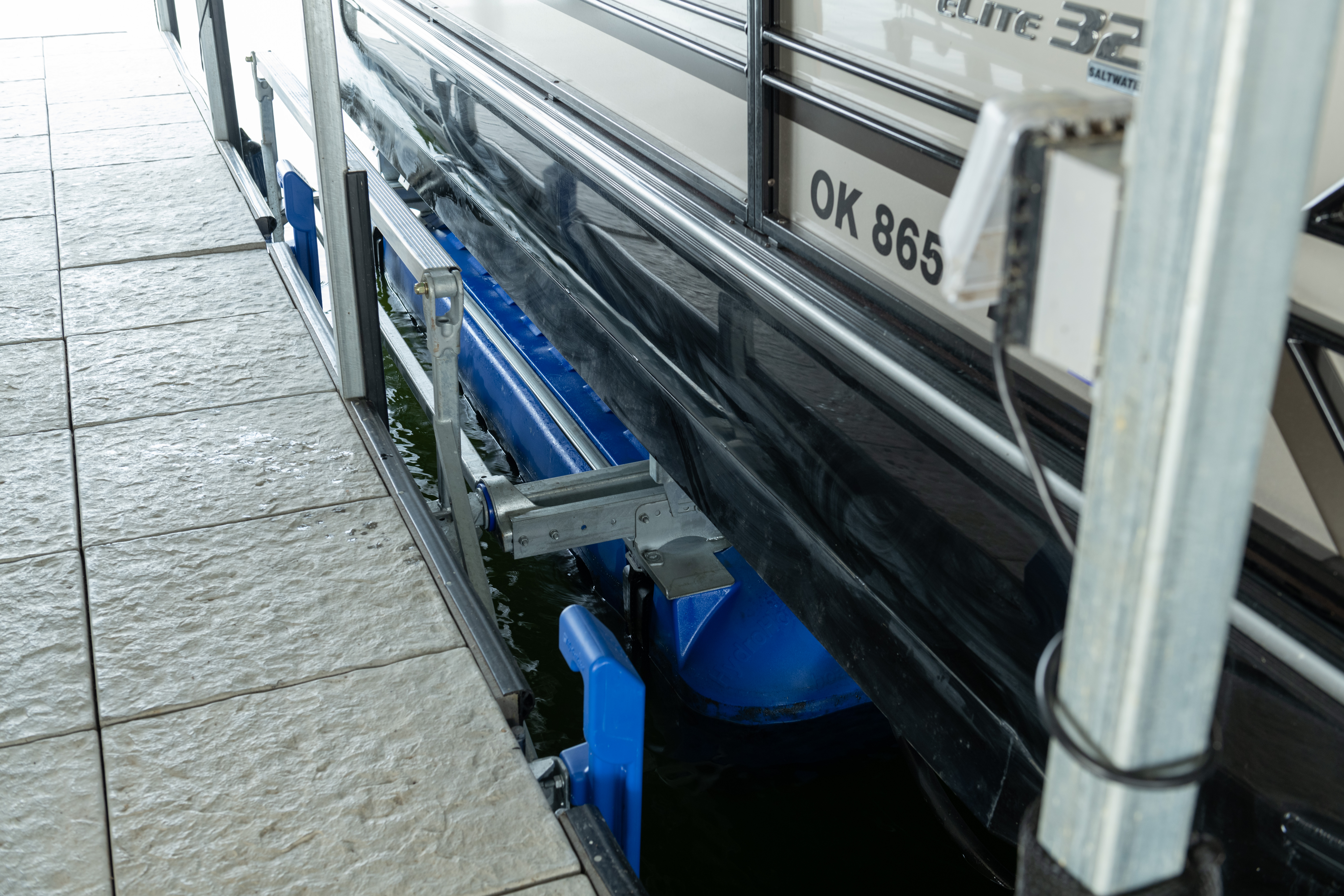 Close-up of a pontoon boat secured on a blue boat lift beside a dock.