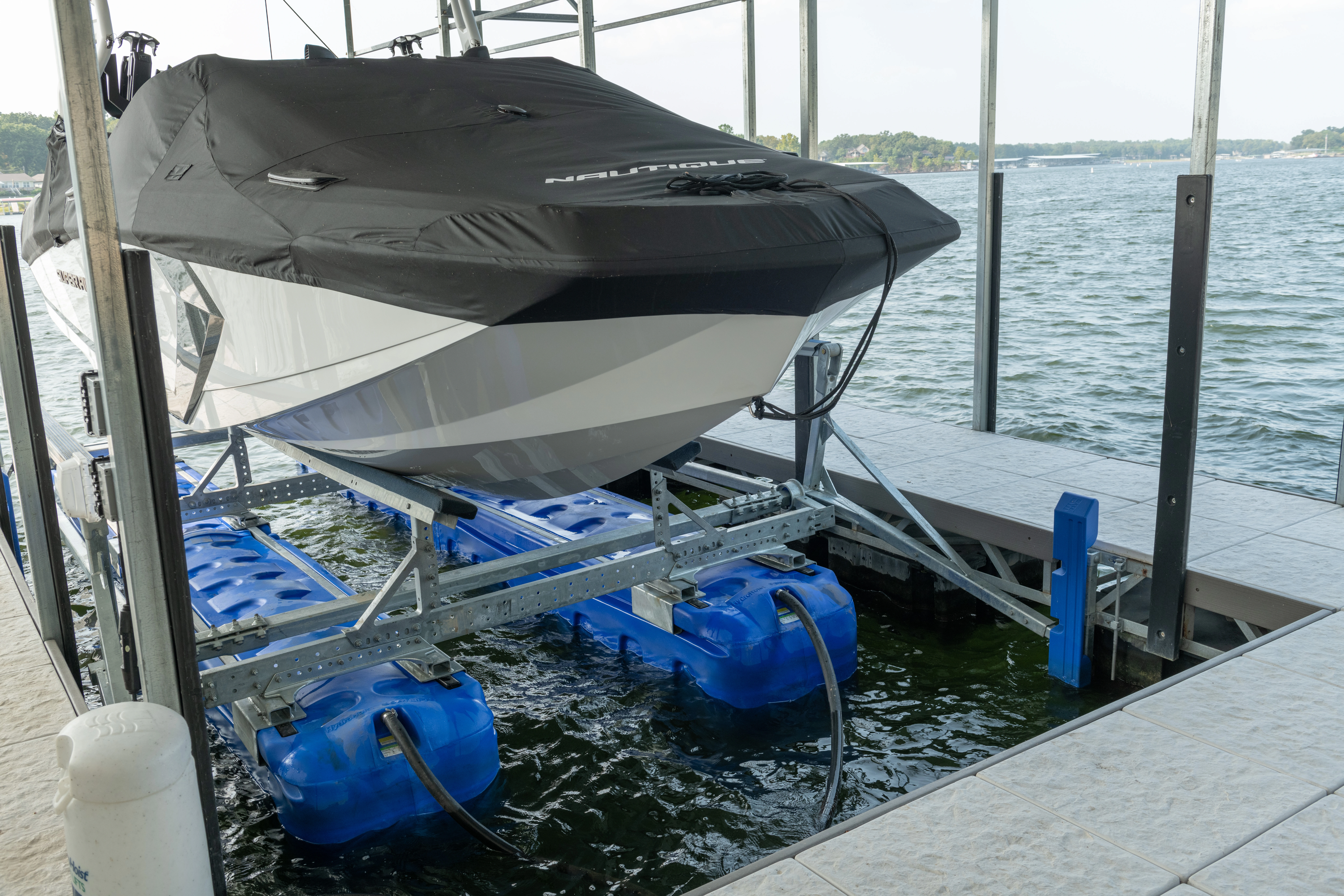 Covered speedboat resting on a floating boat lift with blue flotation tanks beside a dock on a lake.